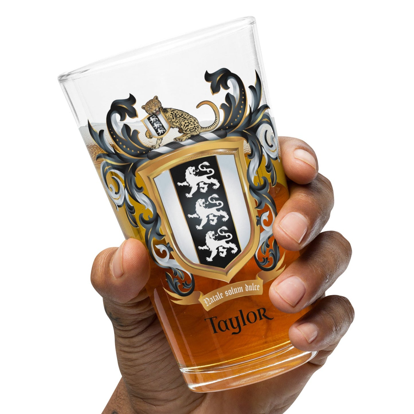 Hand holding a pint glass with a Taylor family crest and the name 'Taylor' in black text below the shield that has 3 white lions on a black and white shield on a white background