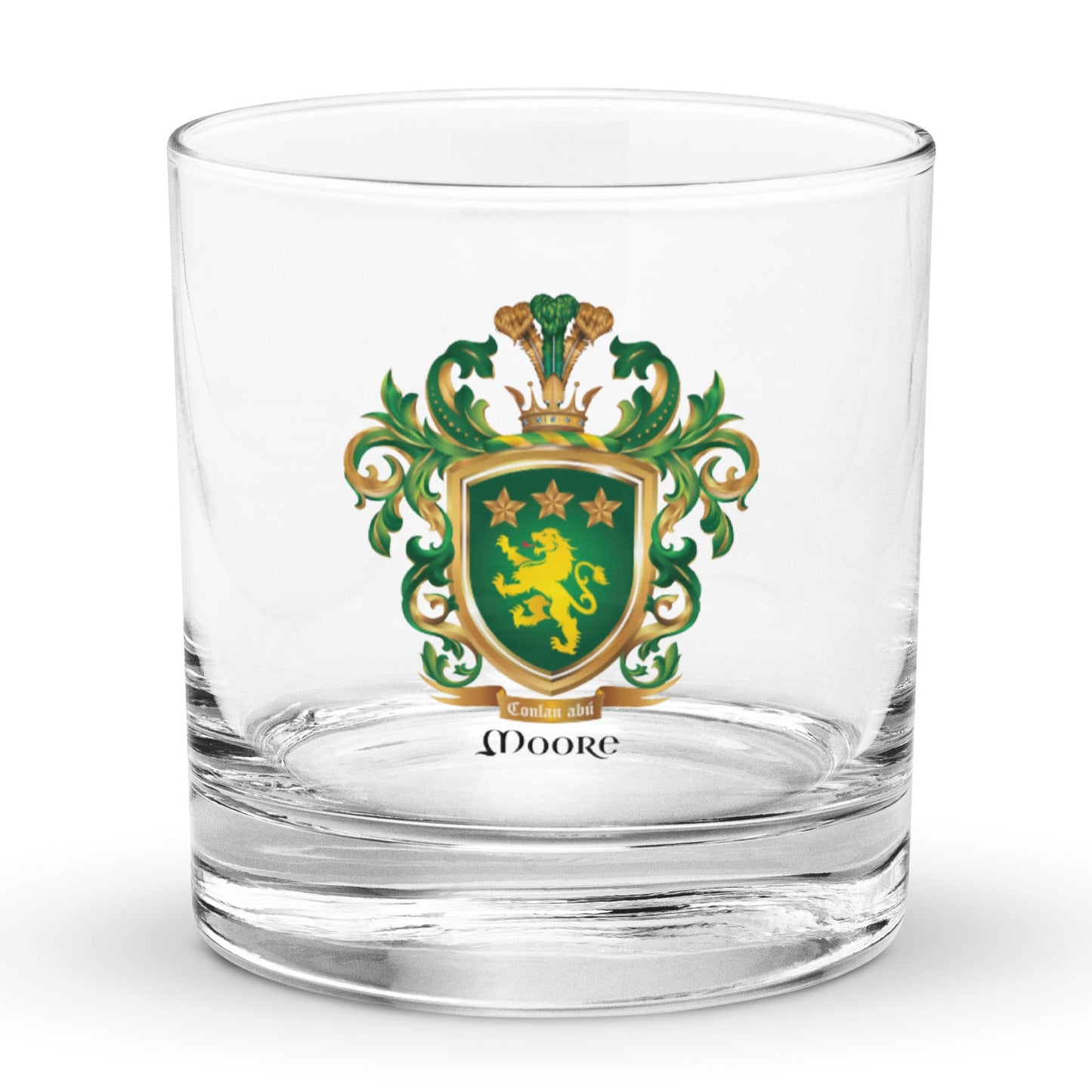 A clear rocks glass featuring The Moore Family Crest showing a green shield with a gold lion and three gold stars above the lion with the motto and Moore name beloe the shield and a crown above and green and gold mantling all around  on a white background