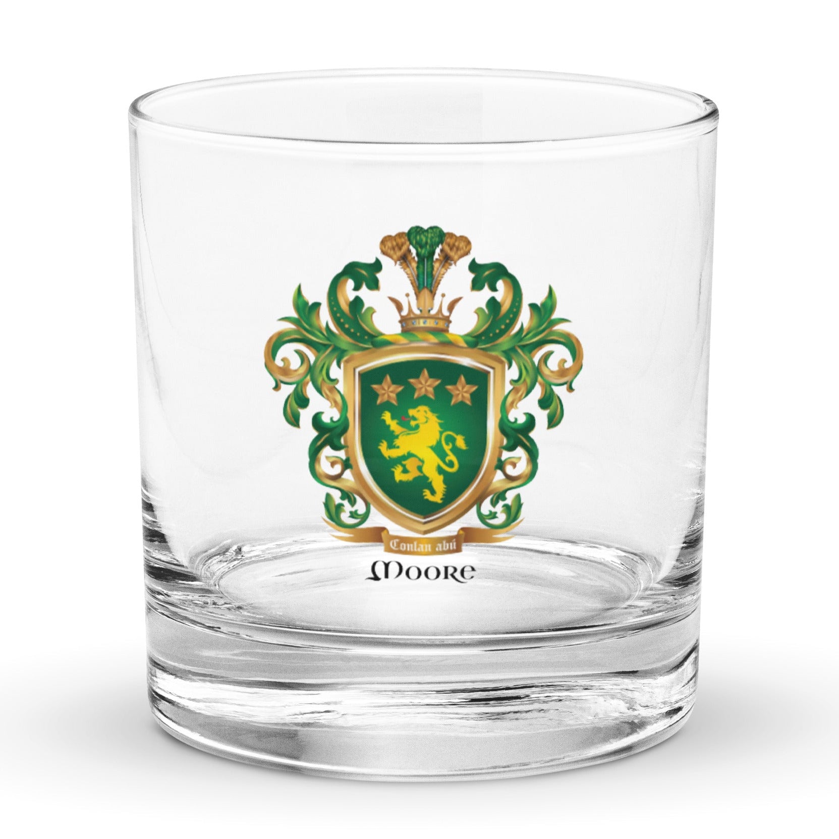 A clear rocks glass featuring The Moore Family Crest showing a green shield with a gold lion and three gold stars above the lion with the motto and Moore name beloe the shield and a crown above and green and gold mantling all around  on a white background