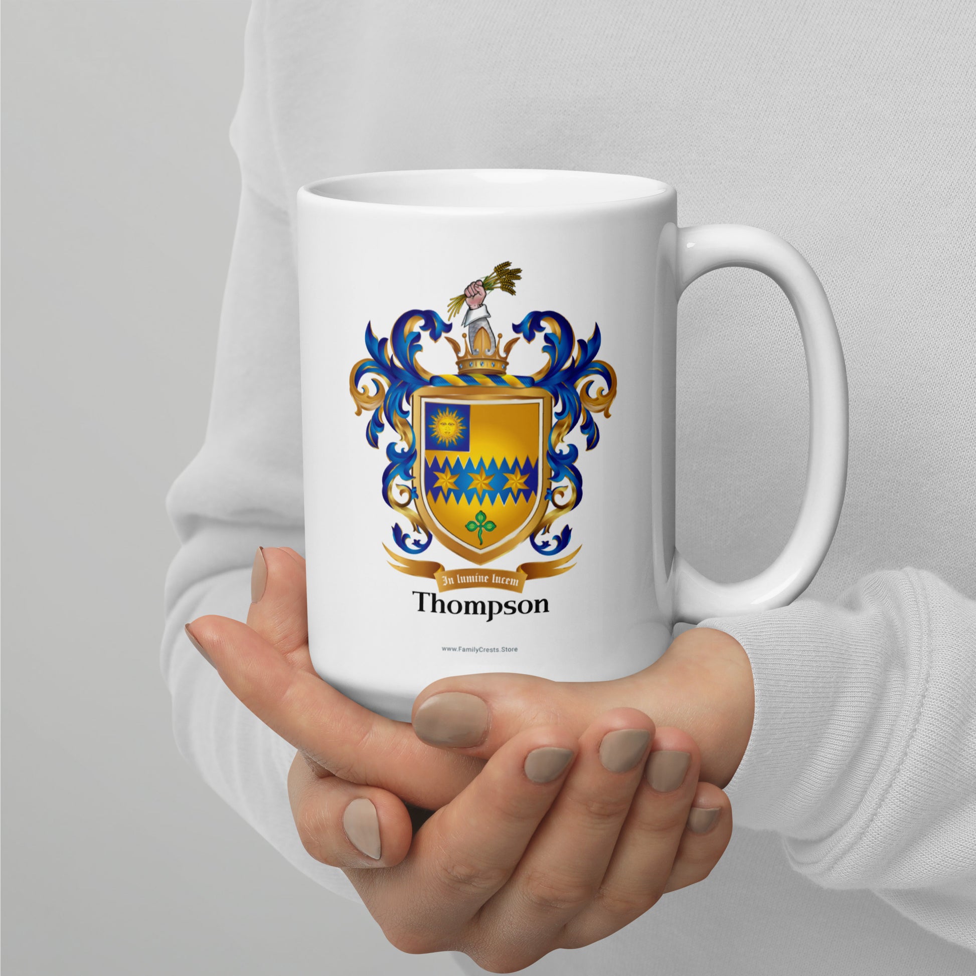 White mug with a family crest and the name 'Thompson' held by a person against a light gray background
