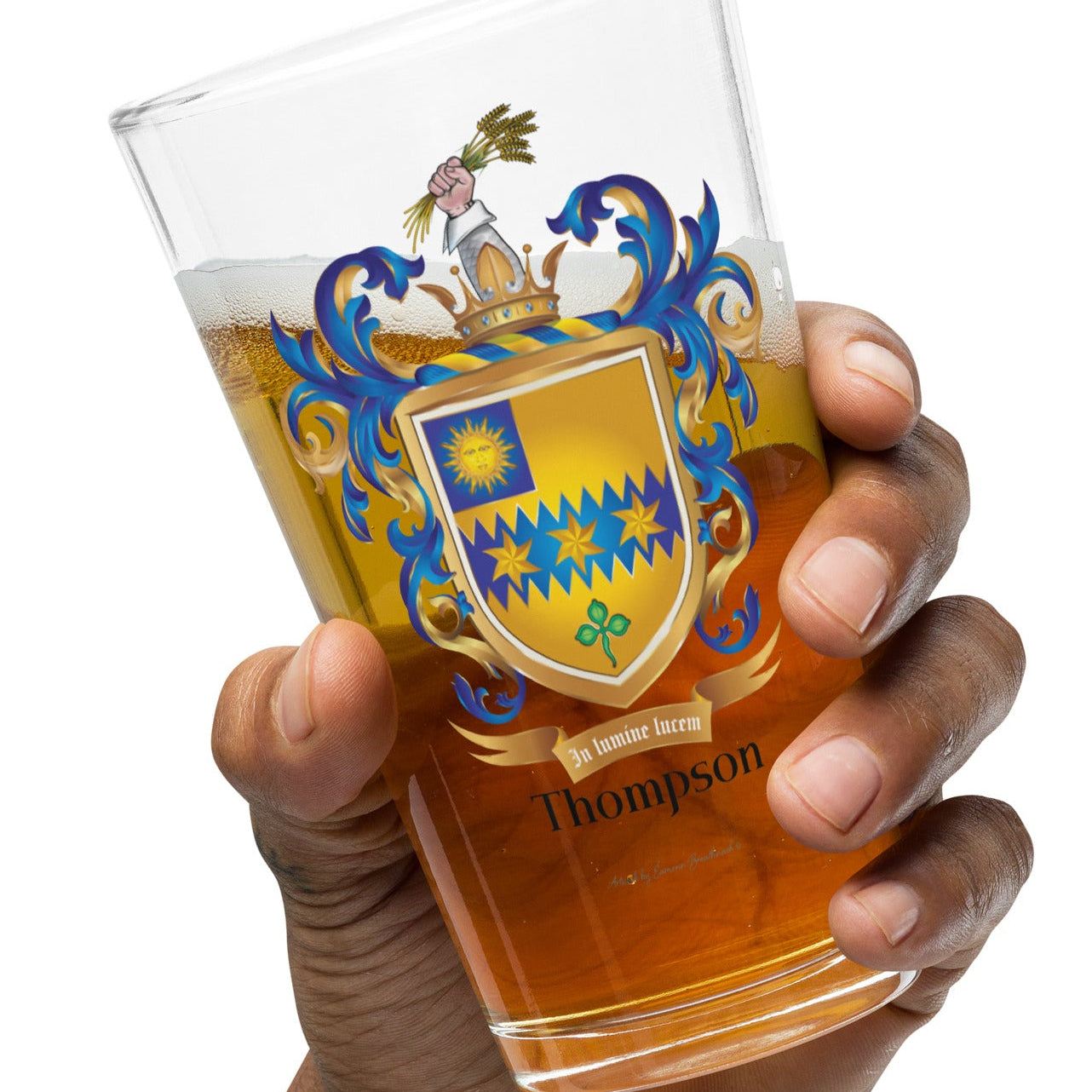 Hand holding a Thompson Family Crest beer glass with beer in the glass showing  'Thompson' word below the crest on a white background