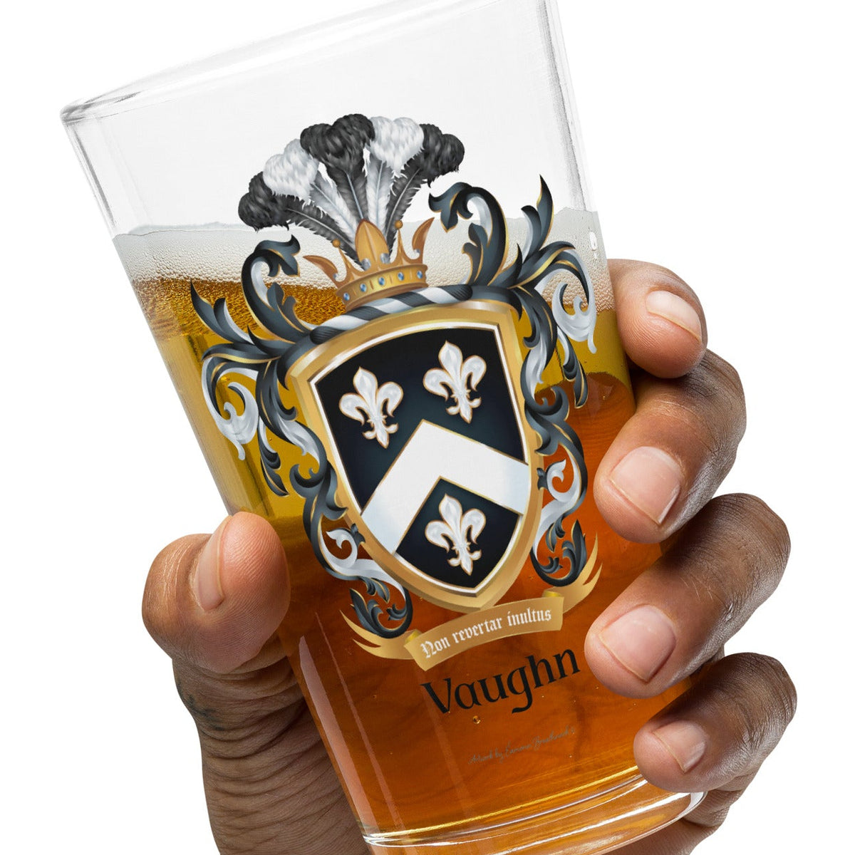 A hand holding a clear pint glass filled with amber beer, featuring a printed black, white, and gold Vaughan crest design on the front, against a solid white background.