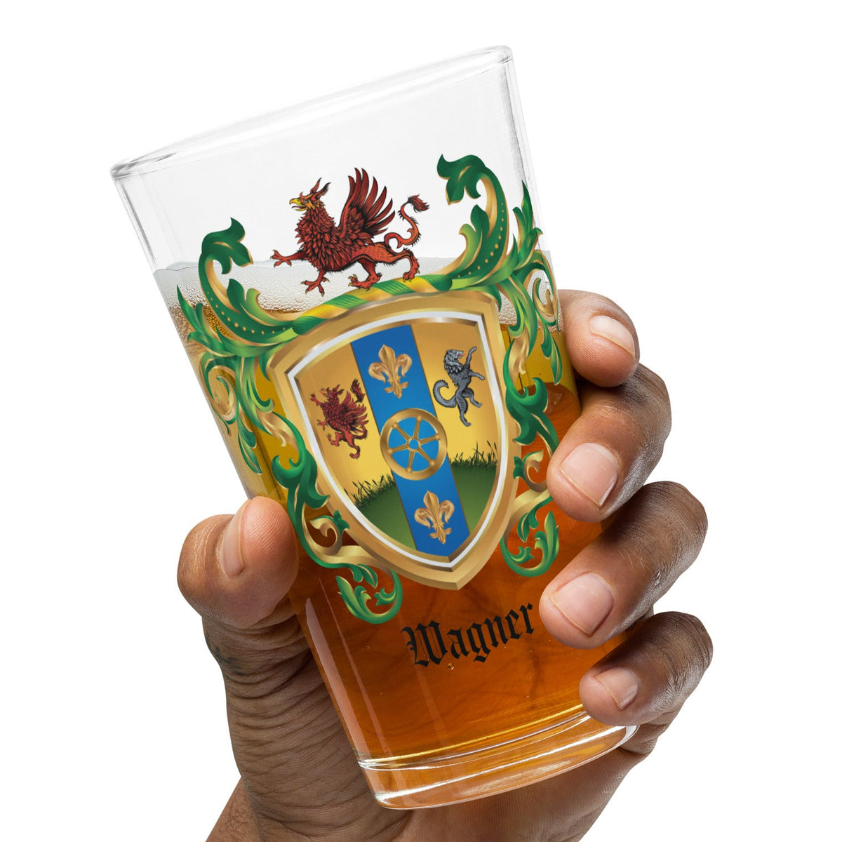 A hand holding a clear pint glass decorated with a detailed heraldic crest,  partially filled with beer, and the name 'Wagner' is printed near the bottom, set against a plain white background.