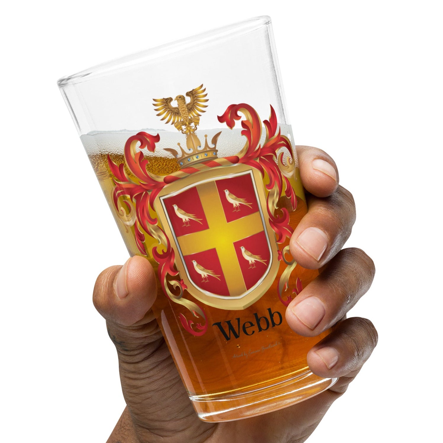 A hand holding a clear pint glass filled with amber beer, featuring a printed Webb coat of arms with a red cross, gold birds, and the name 'Webb' at the bottom, against a plain white background.