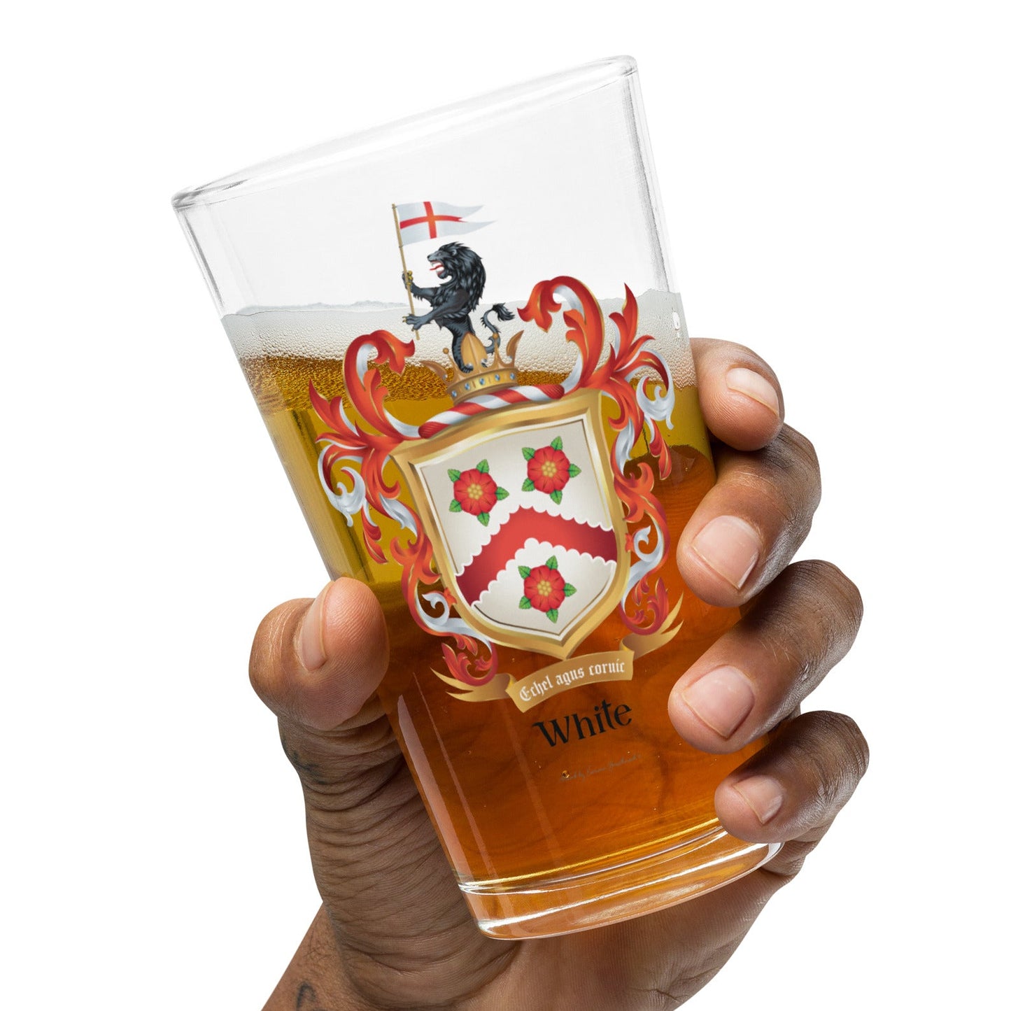 A hand holding a clear pint glass filled with beer, featuring the White Family Crest, against a plain white background.