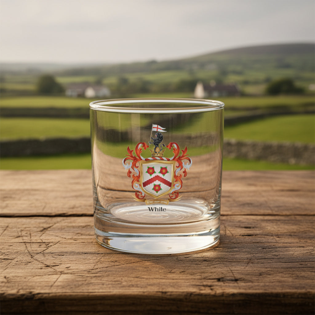 A clear glass rocks tumbler with a White-Family-Crest on a wooden table with a rural Irish background of fields and stone walls.