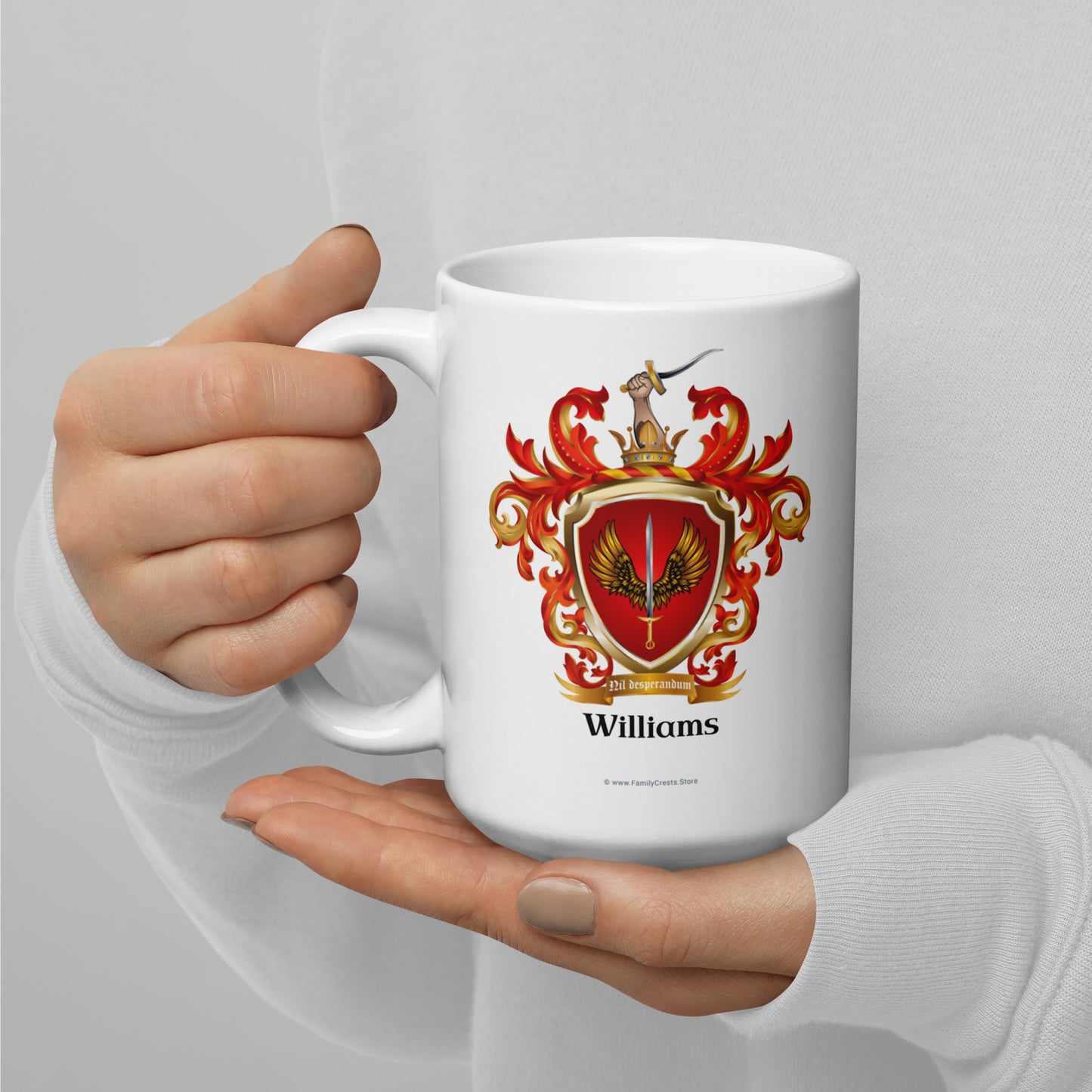 White mug with a red and gold coat of arms design and 'Williams' text, held by a hand against a light gray background.