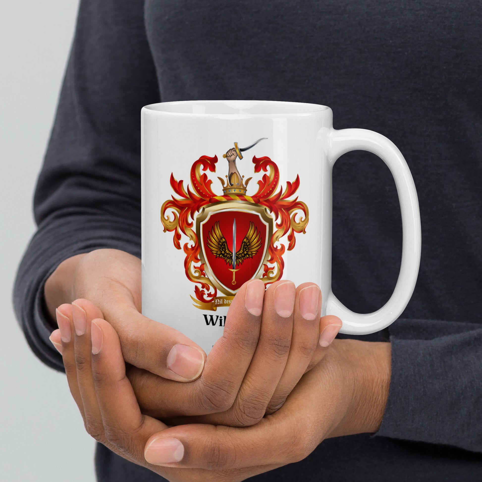 Person holding a white mug with a red and gold Williams Family Crest on a gray background