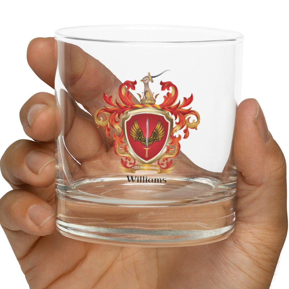 Clear rocks glass with a Williams Family Crest held in a hand against a white background