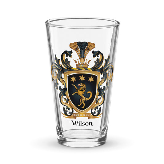 A clear pint beer glass with the Wilson Family Crest featuring a golden wolf with 3 stars on a black shield photographed on a white background
