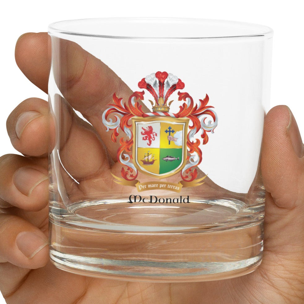Hand holding a rocks glass with a McDonald coat of arms design on a white background