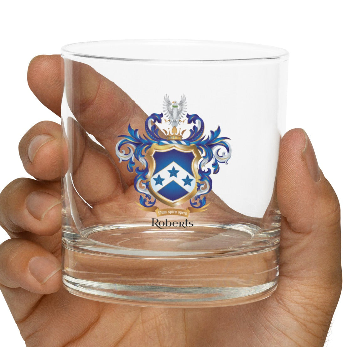 Hand holding a clear glass with a Roberts coat of arms design on a white background